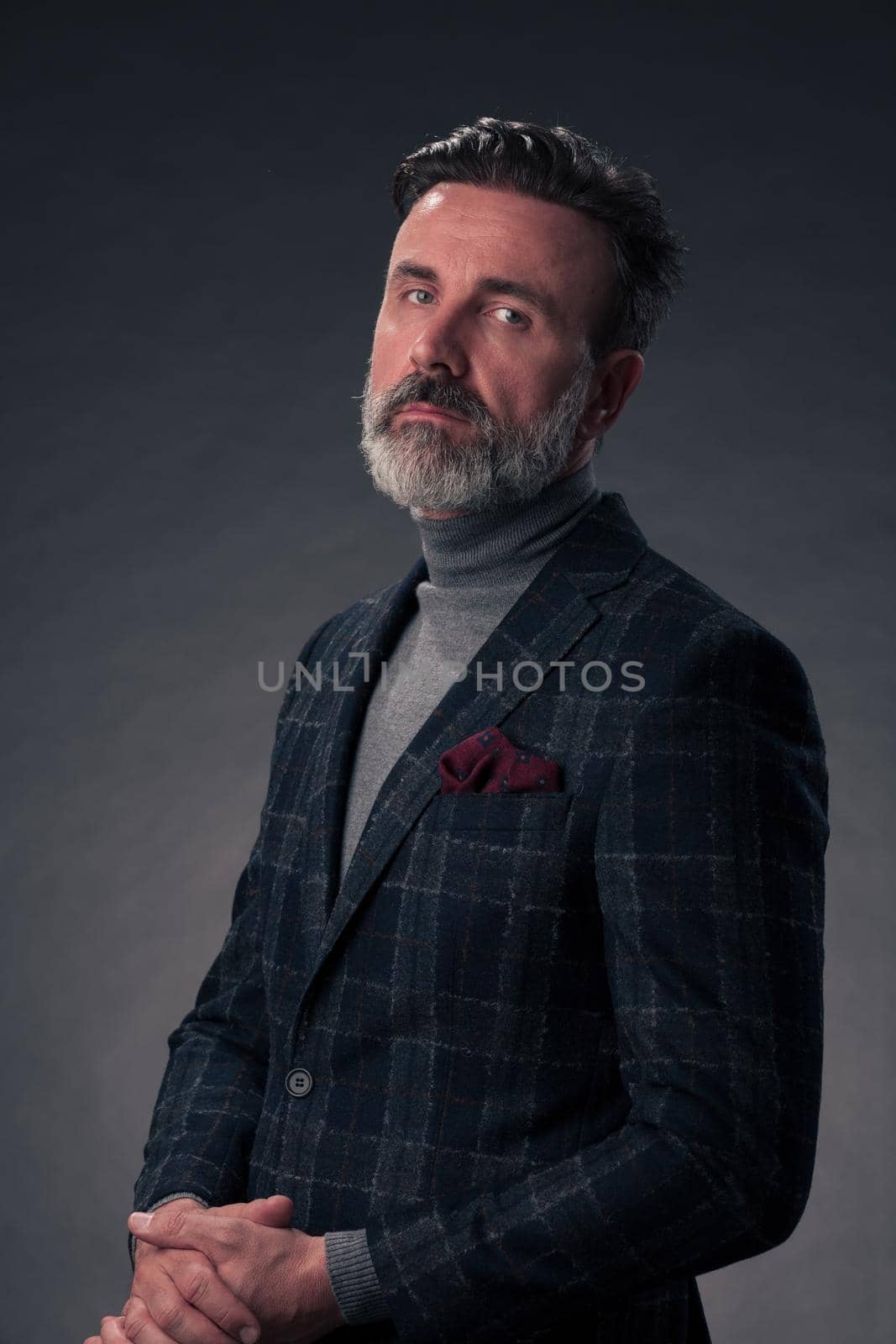 Portrait of a successful stylish elegant senior businessman with a grey beard and casual business clothes confident in photo studio isolated on dark background gesturing with hands. High-quality photo