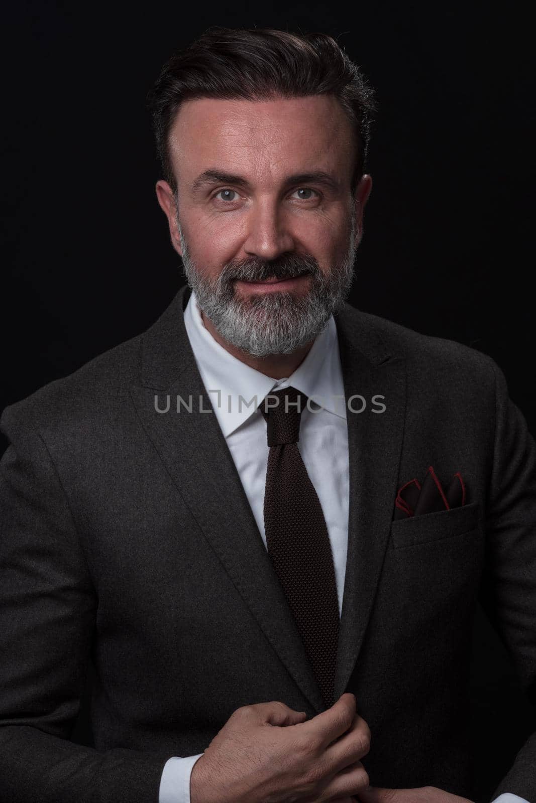 Portrait of a successful stylish elegant senior businessman with a grey beard and casual business clothes confident in photo studio isolated on dark background gesturing with hands. High-quality photo