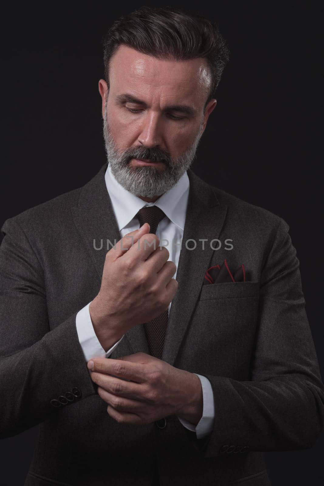 Portrait of a successful stylish elegant senior businessman with a grey beard and casual business clothes confident in photo studio isolated on dark background gesturing with hands. High-quality photo