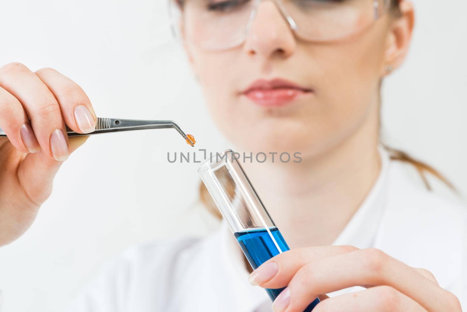 Scientist puts sample into test tube with liquid. Biochemistry laboratory analysis and experimentation. Closeup woman hands holding test tube and tweezers. Biology researching and lab testing.