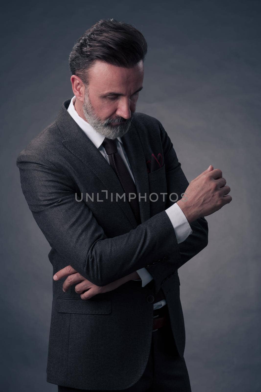 Portrait of a successful stylish elegant senior businessman with a grey beard and casual business clothes confident in photo studio isolated on dark background gesturing with hands. High-quality photo