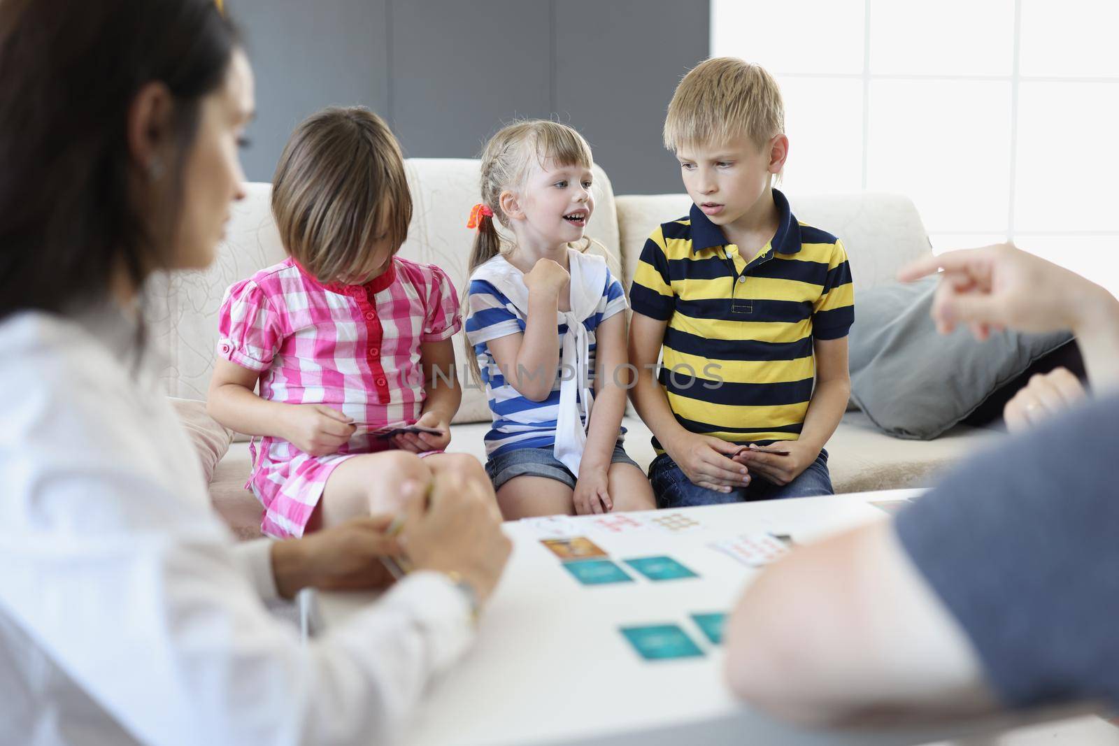 Portrait of children decide who goes next, playing card game with parents at home. Adults teach kids how to play. Pastime, education, development concept