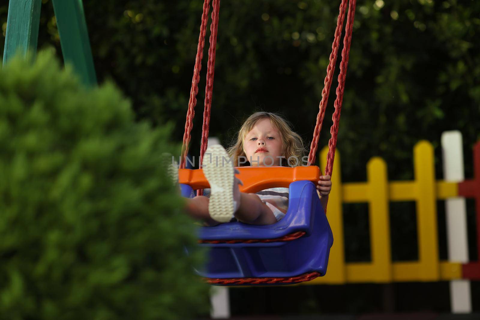 Little girl having fun on swing on playground in park alone by kuprevich