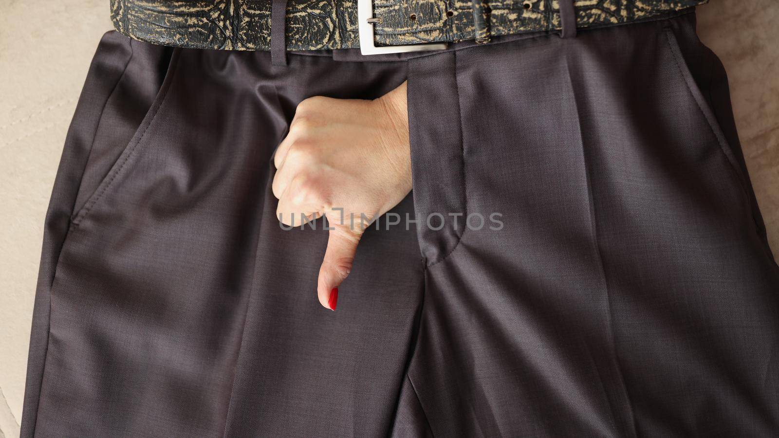 Top view of woman show thumbs down gesture through mans pants. Fun of masculinity, joke about manhood. Sign of impotence, infertility, size matter concept