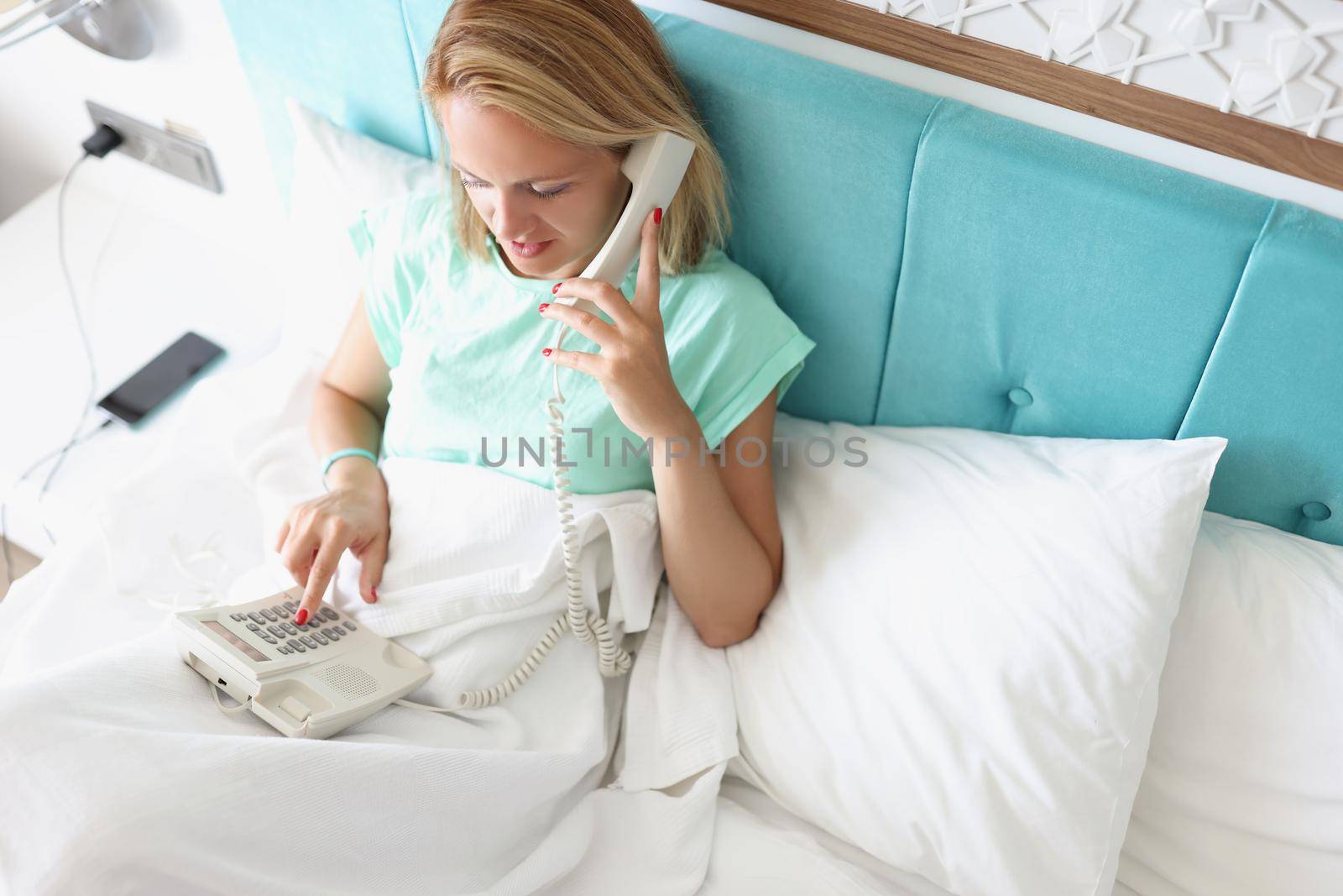 Top view of young woman calling on reception in hotel to order breakfast in room. Female enjoy luxury service on resort. Holiday, chill, lunch time concept