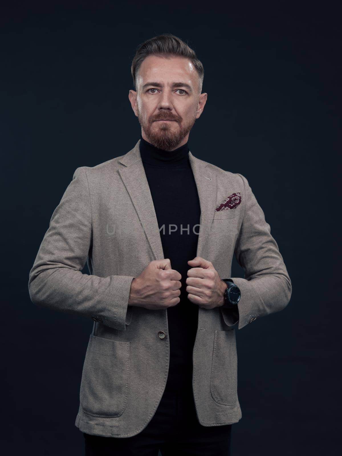 Portrait of a successful stylish elegant senior businessman with a grey beard and casual business clothes confident in photo studio isolated on dark background gesturing with hands. High-quality photo