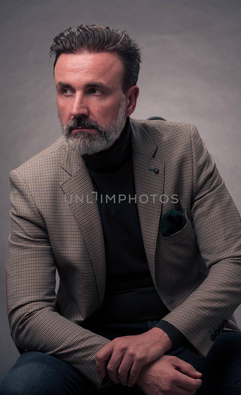 Portrait of a successful stylish elegant senior businessman with a grey beard and casual business clothes confident in photo studio isolated on dark background gesturing with hands. High-quality photo