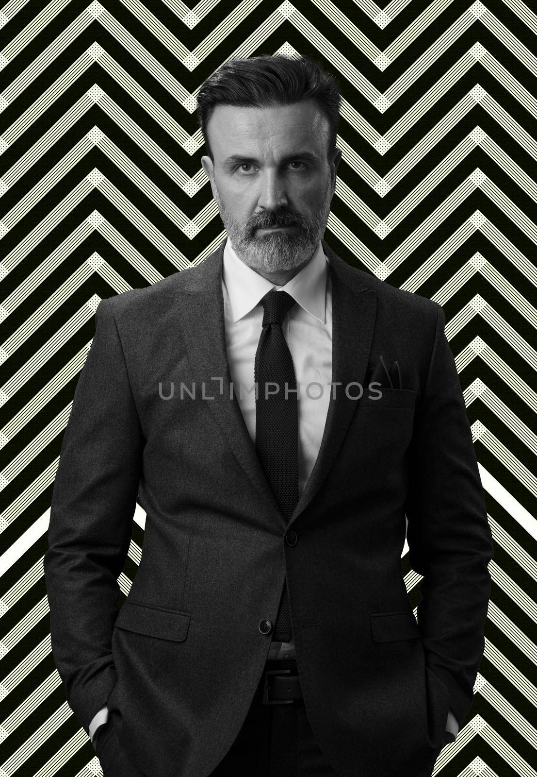 Black and white portrait of a stylish elegant senior businessman with a beard and casual business clothes against retro colorful pattern design background gesturing with hands by dotshock