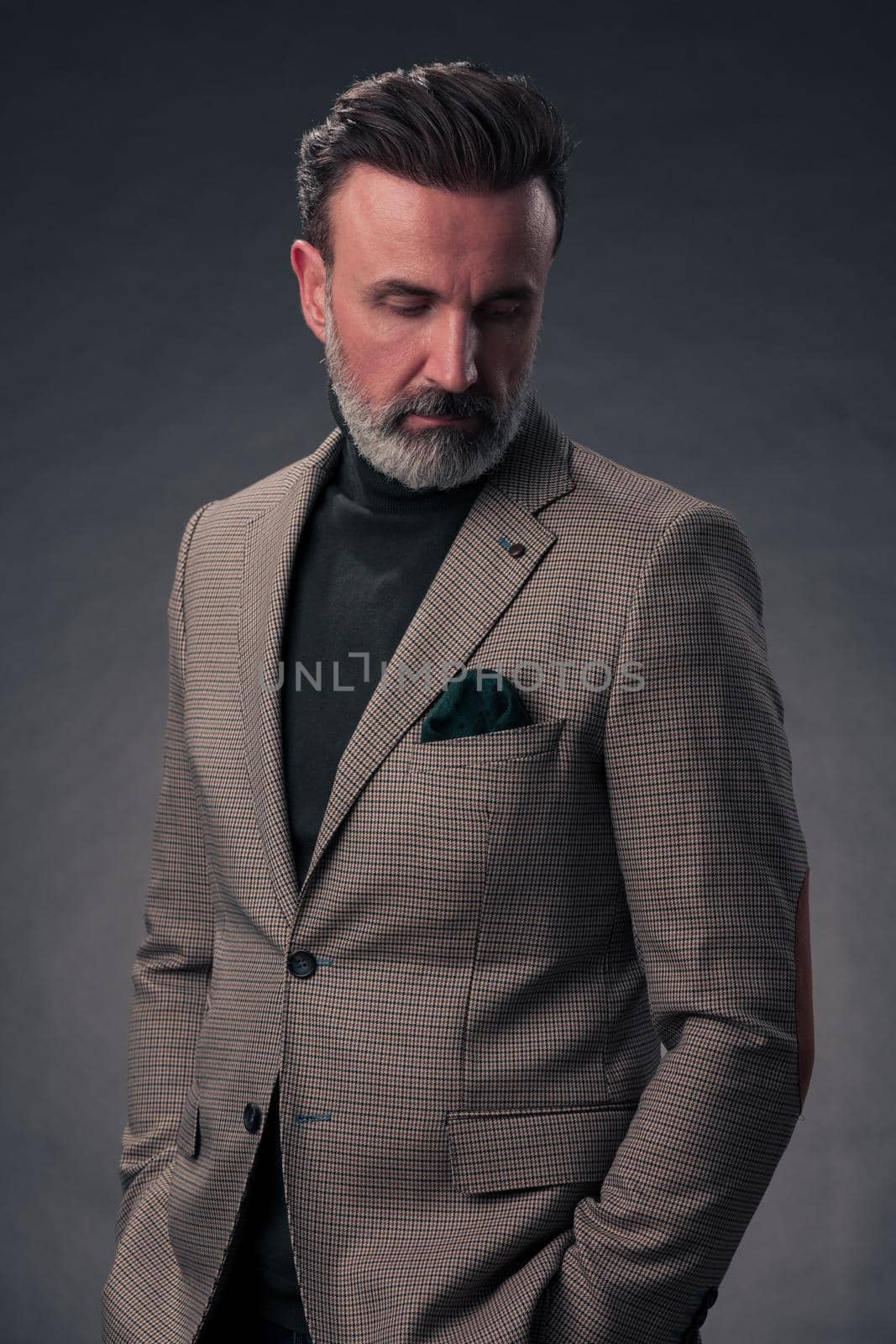 Portrait of a successful stylish elegant senior businessman with a grey beard and casual business clothes confident in photo studio isolated on dark background gesturing with hands. High-quality photo