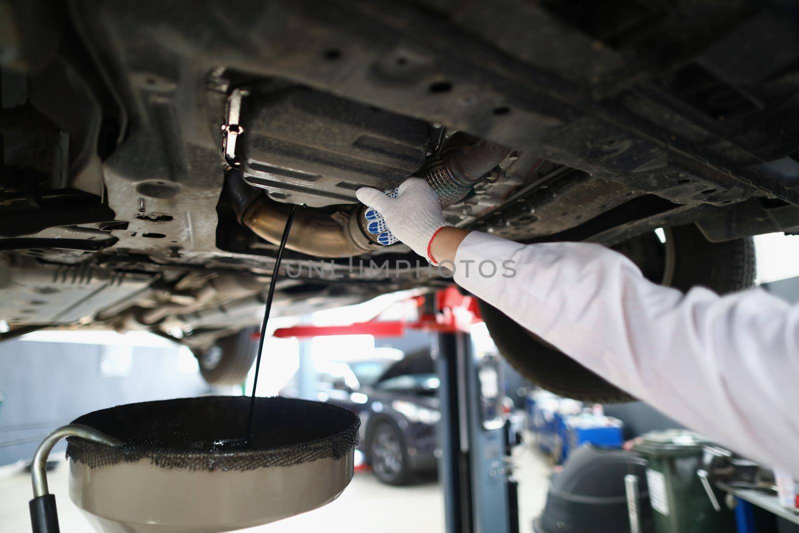 Close-up of mechanic man on car maintenance service change oil under transport. Garage with professional help and workers. Pit stop, fixing service concept