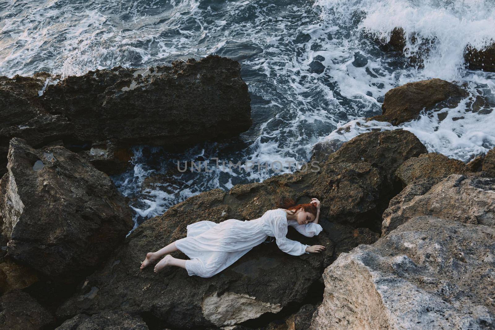 Barefoot woman in a secluded spot on a wild rocky coast in a white dress vacation concept. High quality photo