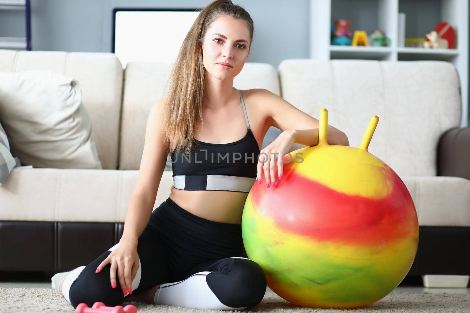 Portrait of attractive young woman pose with dumbbells and ball on floor. Girl prepare for active workout at home. Sport, physical activity, hobby concept