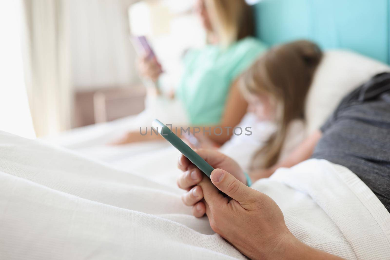 Close-up of man holding smartphone and reading news in morning in bed. Person addicted to modern device, kill time, bored. Technology, addiction concept