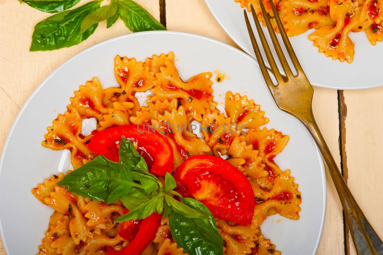 Italian pasta farfalle butterfly bow-tie with tomato basil sauce over white rustic wood table