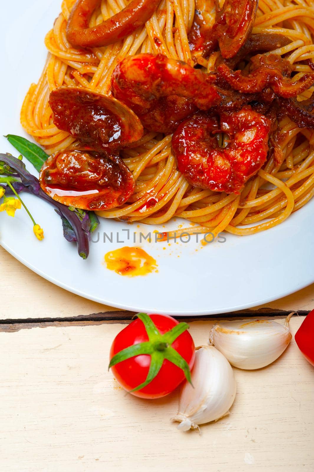 Italian seafood spaghetti pasta on red tomato sauce over white rustic wood table