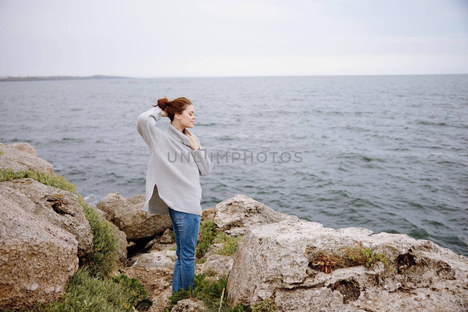 pretty woman in a gray sweater stands on a rocky shore nature Lifestyle by SHOTPRIME