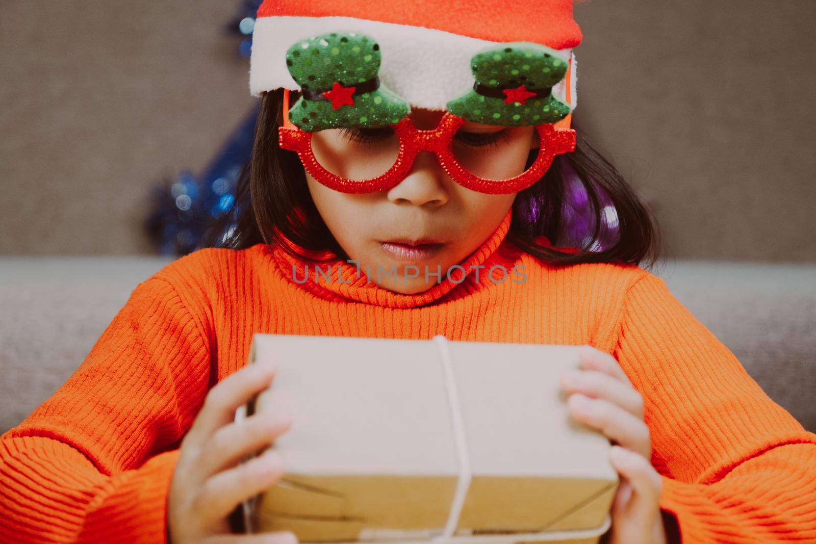 Happy little girl in Santa hat with christmas gift box at home. Happy New Year and Merry Christmas.