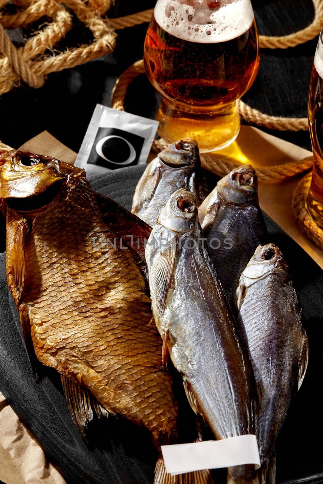 Various appetizing whole air-dried and smoked fish served on black wooden board with foamy amber lager. Popular complements to beer concept