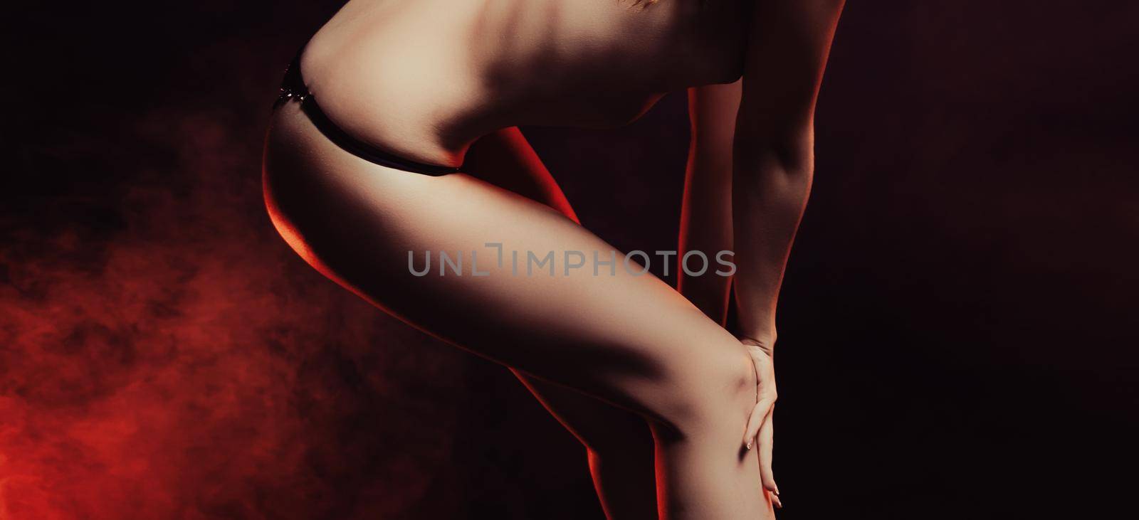 Young semi-nude woman in lace black panties posing in the studio on a dark background