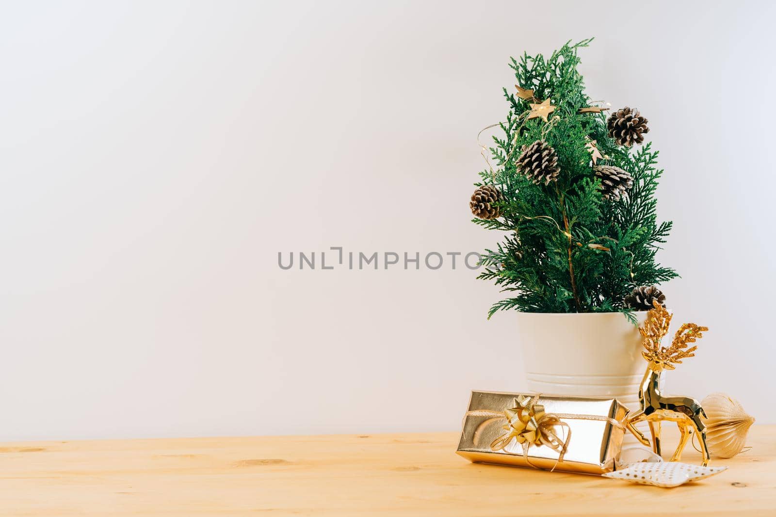 Creative natural miniature Christmas tree in pot on wooden table with gift boxes and white background. Xmas greeting card with copy space. Happy New Year