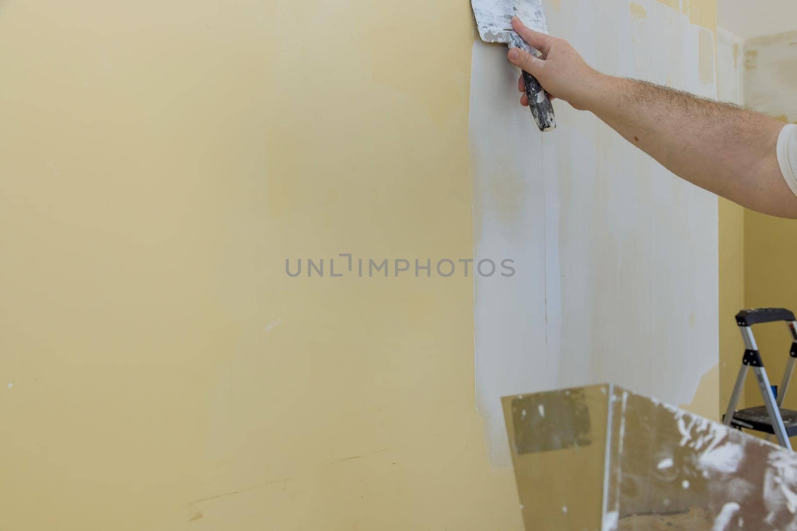 Man plastering the walls with finishing putty in room with putty spatula of repair work construction