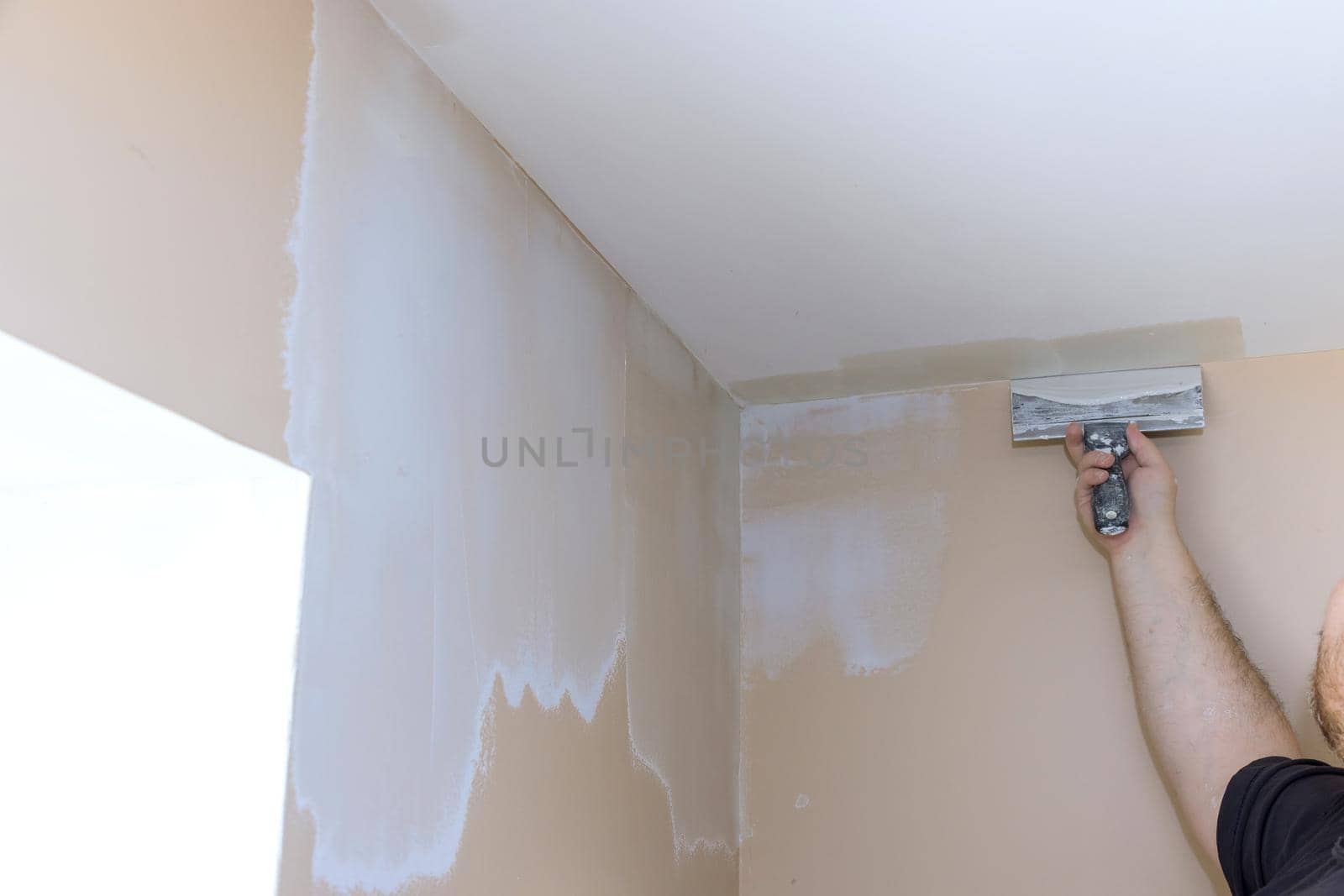 Plasterer smoothing wall surface with putty knife at home by ungvar