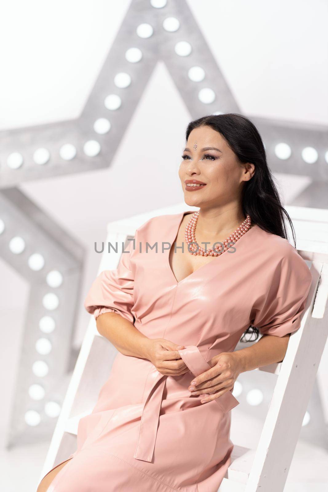 Asian Fashion Woman Posing at the Art Film Studio. Asian Woman With Bindi on her Forehead Against the Backdrop of Fashion Scenery. Close-up portrait. White star lights background by LipikStockMedia