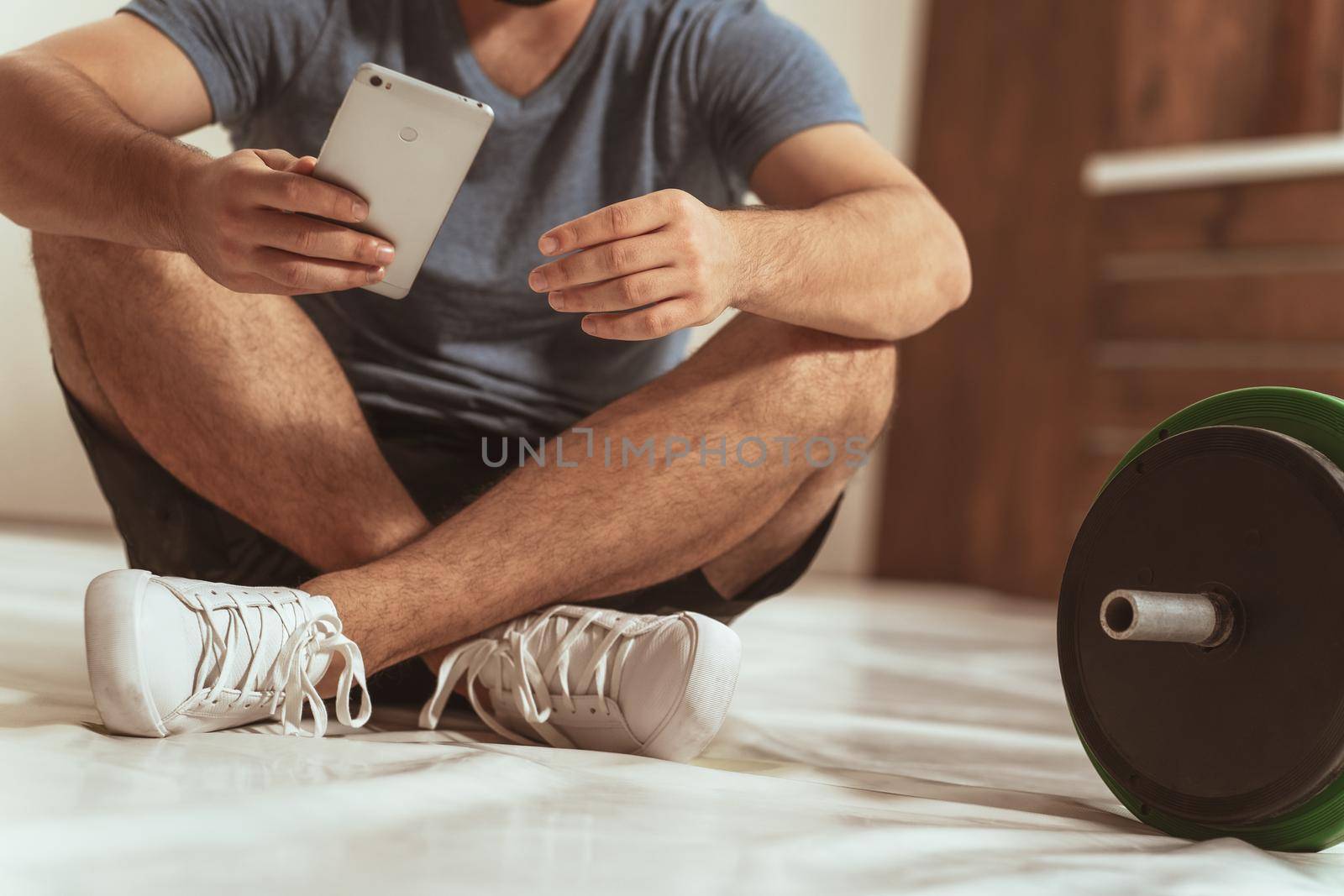 No face visible young man having a break sitting on a floor with black and green tone fitness barbell, equipment for weight training concept. Male sports equipment for training.