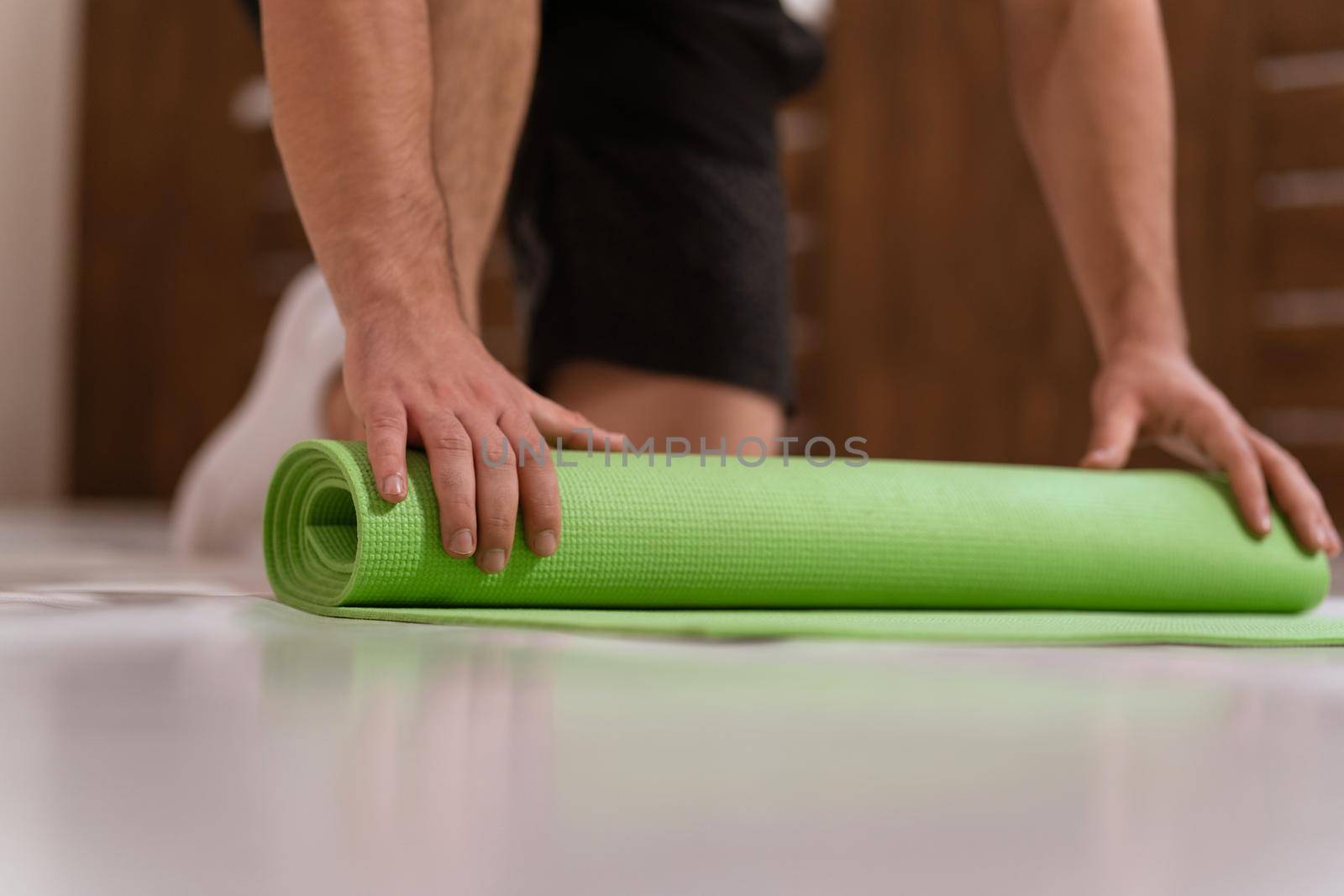 Unwinding roll mat, preparing a place for sports fitness man. Determined guy doing physical training. Strong handsome young man, an a gym by LipikStockMedia
