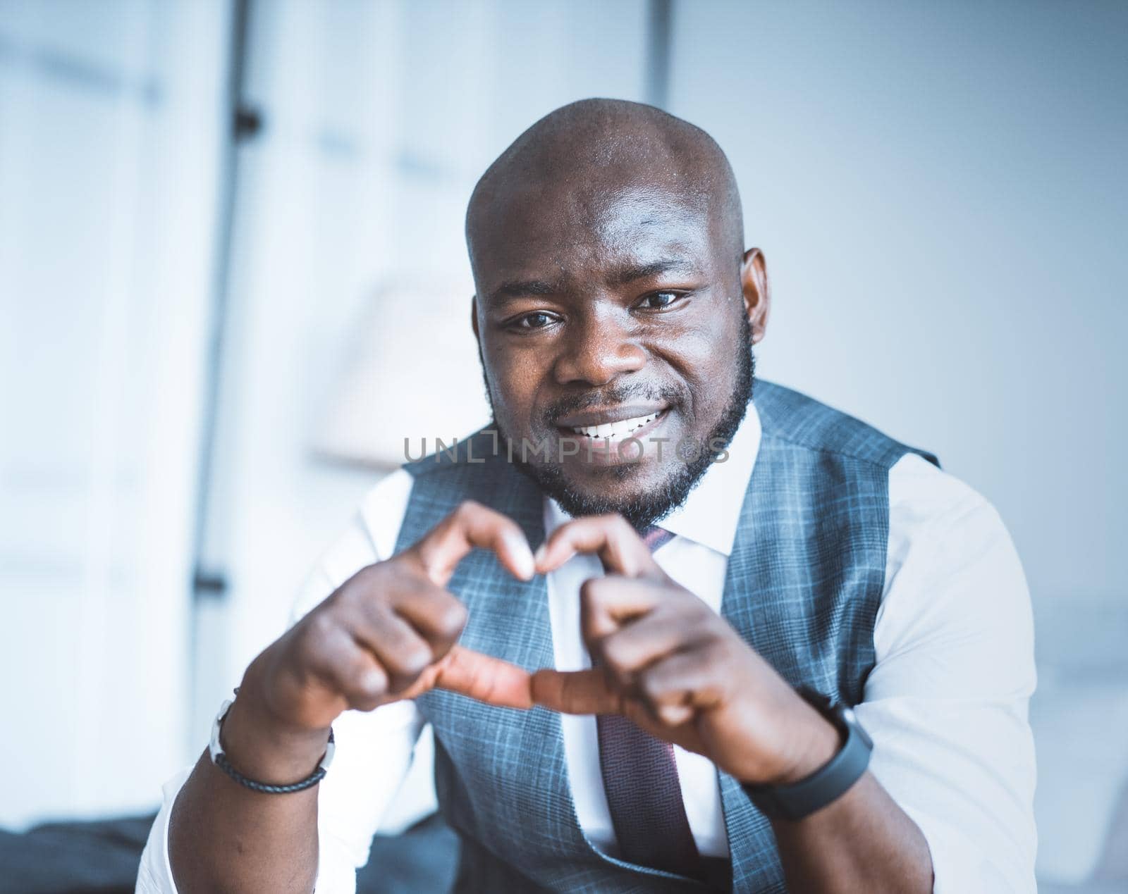 Romantic Office Manager Makes Heart of his Fingers and his eyes are Full of Love. Charming Guy Shows Heart-hand Symbol Close-up Portrait. Blurred Background. High quality photo