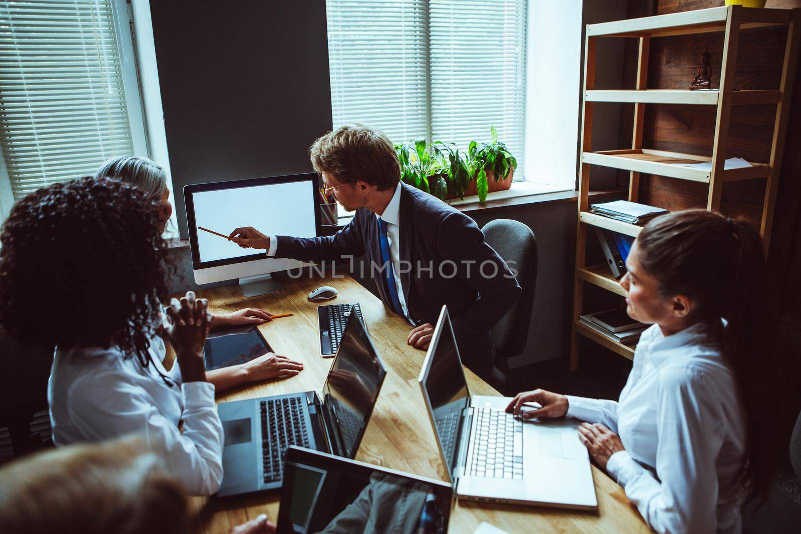 Young group of multi ethnic business people looking at computer with white screen at meeting. Supervisor of project showing info on screen of desk top computer. Toned image.
