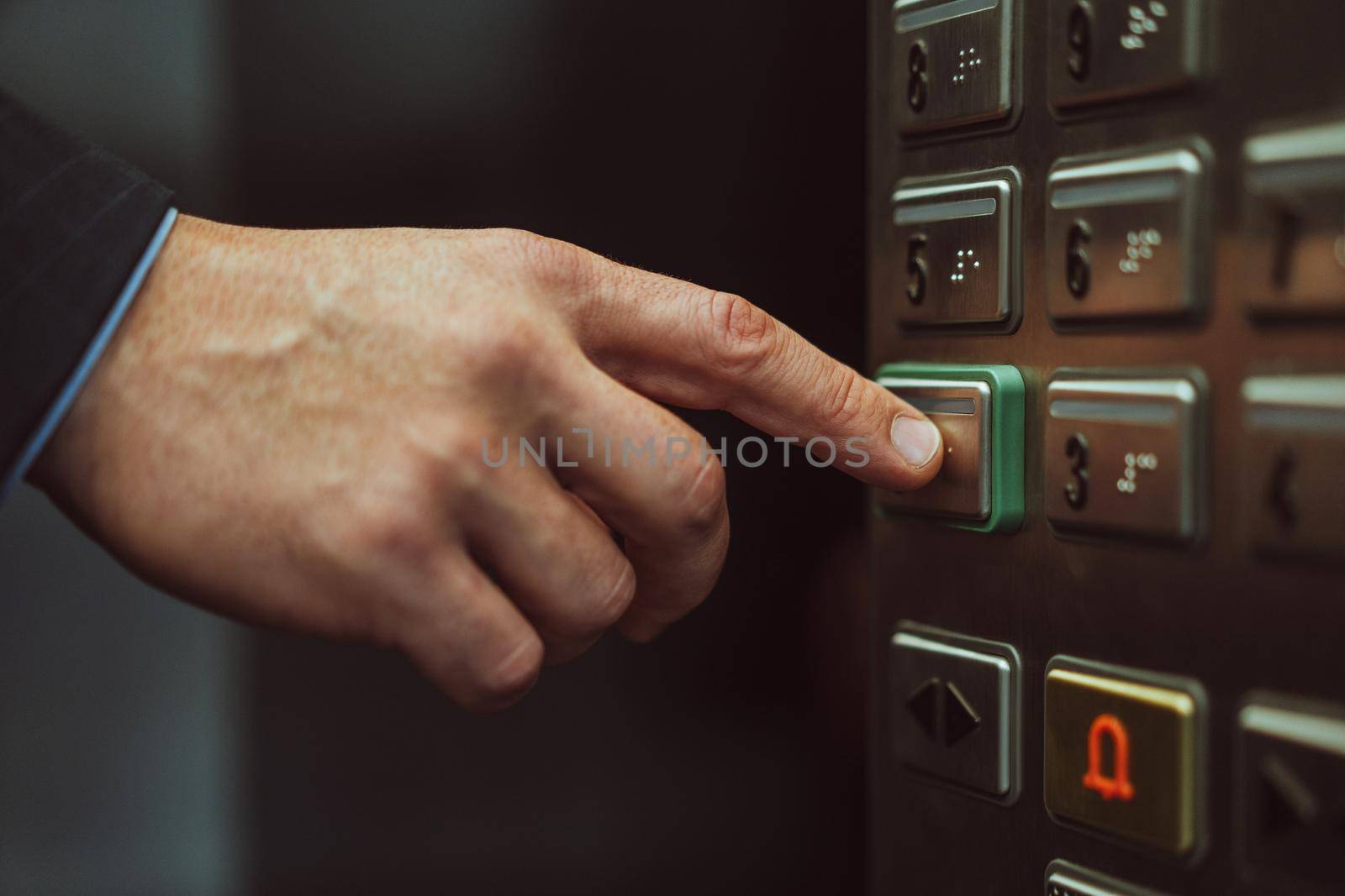 Close up of male hand presses button with braille for blind. Close up shot. Hand of office worker in business suit press the elevator button with his finger. Businessman in an office center.