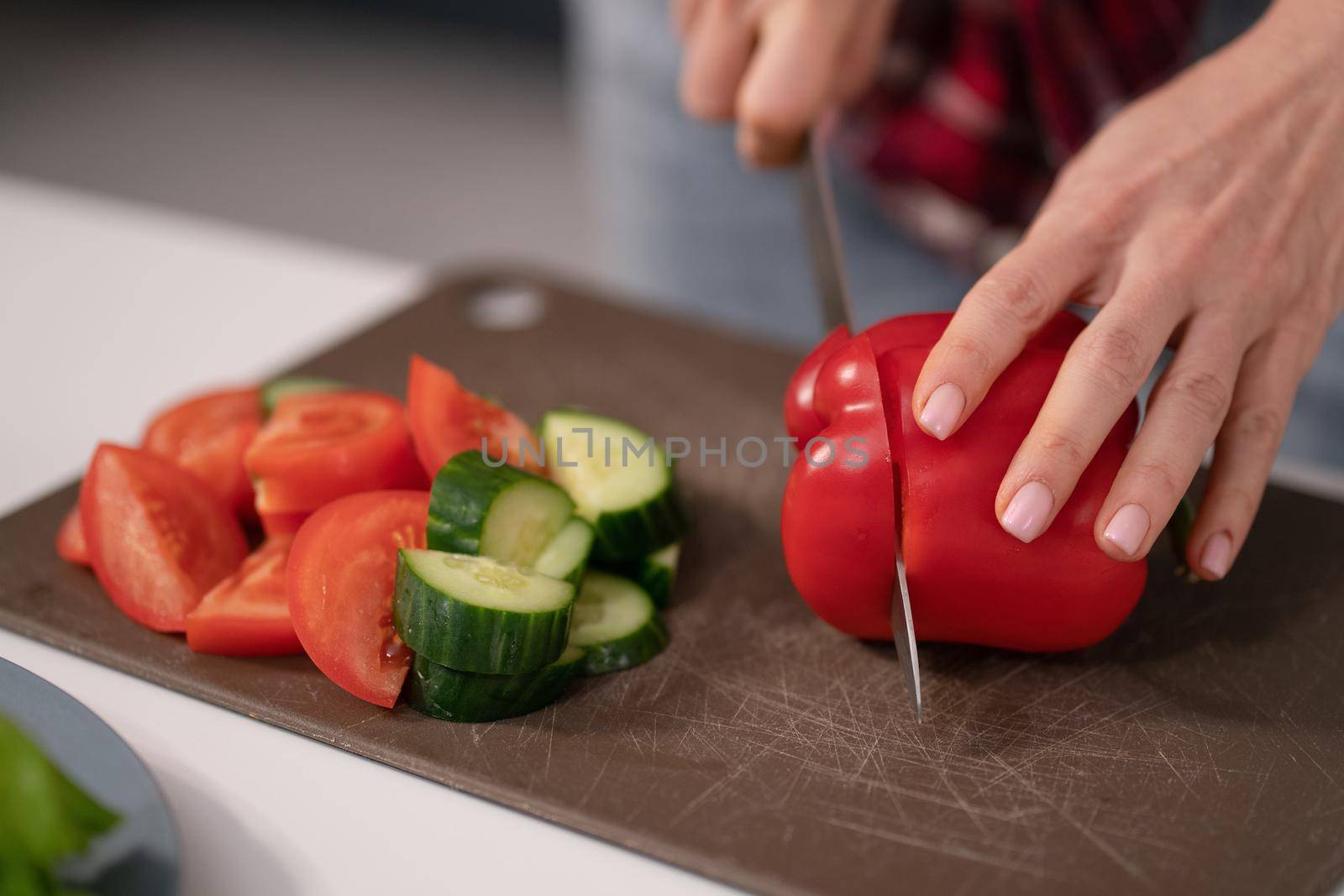 Cutting in slices a fresh vegetable salad young housewife cut sweet pepper, cucumber, tomato on board preparing for a family dinner standing in the kitchen. Healthy food living. Healthy lifestyle.