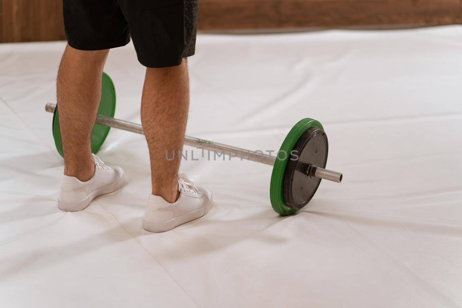 Weightlifting young man taking a brake standing near black and green weight set, equipment for weight training concept. Sports equipment for training. Weight loss, healthy lifestyle concept.