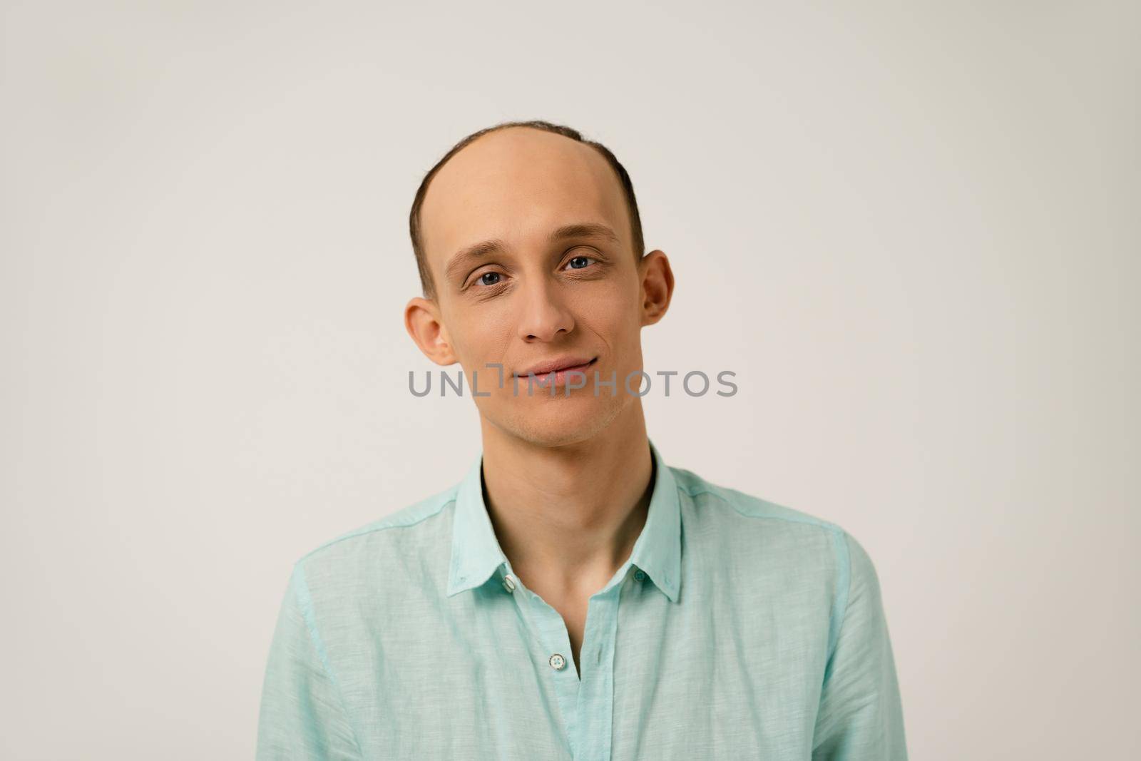 Portrait of young bald man with funny protruding ears in coral blue shirt with looking at camera isolated over white background in studio. Hair loss concept.
