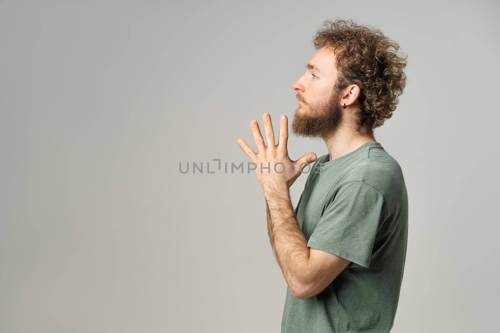 Young handsome man casual sideways pose with palms folded. Handsome young man with curly hair in olive t-shirt looking at camera isolated on white background.