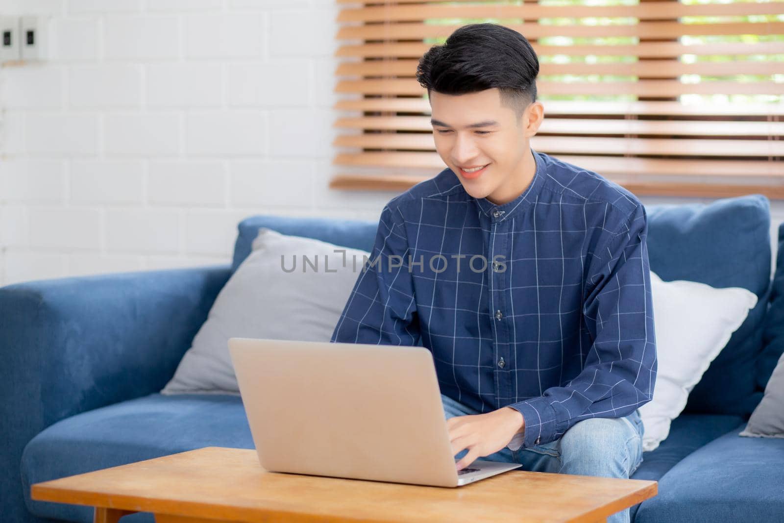 Young asian man typing keyboard on laptop computer on desk at home, businessman working to internet online, freelance male using notebook on table, communication and lifestyle concept.
