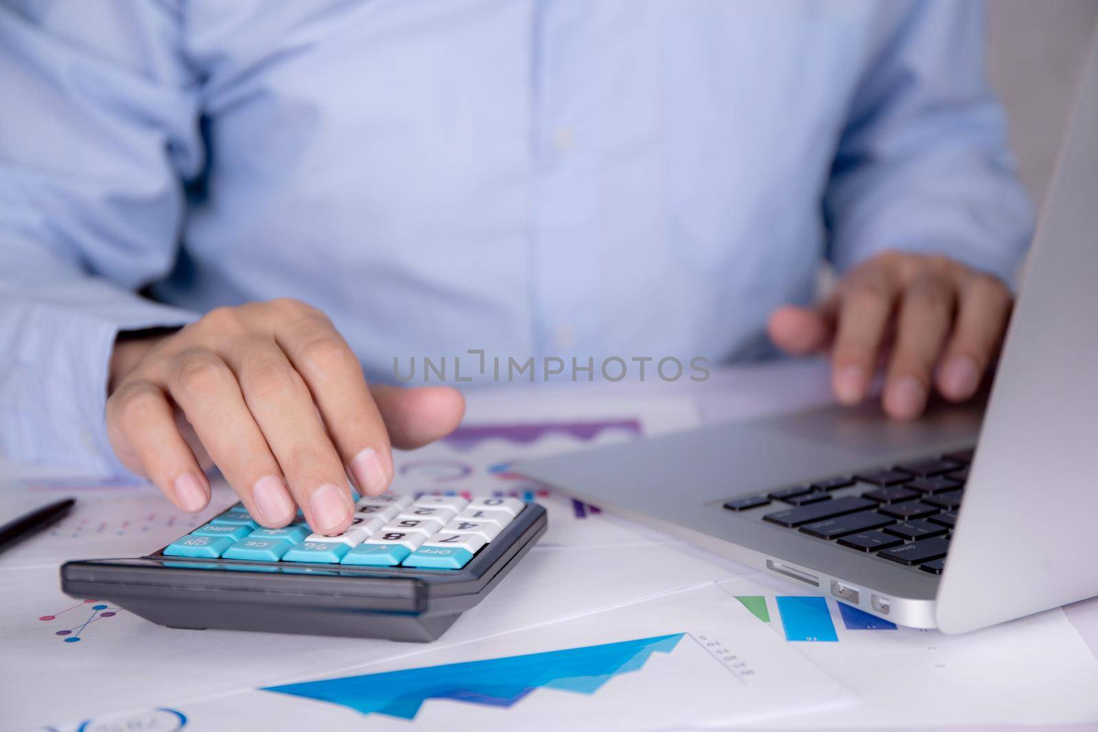 Hands of businessman calculate tax with calculator while laptop computer on desk, man planning finance and investment with graph and chart, statistic and examining account, business concept.