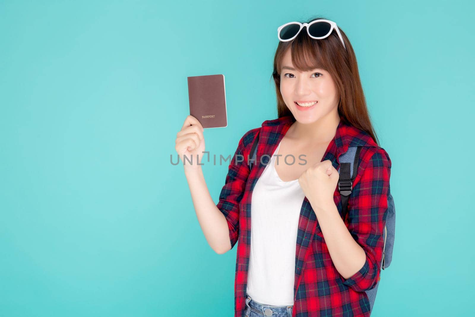 Beautiful portrait young asian woman wear sunglasses on head smile excited and enjoy summer holiday isolated blue background, asia girl hipster cheerful holding passport for travel trip concept.