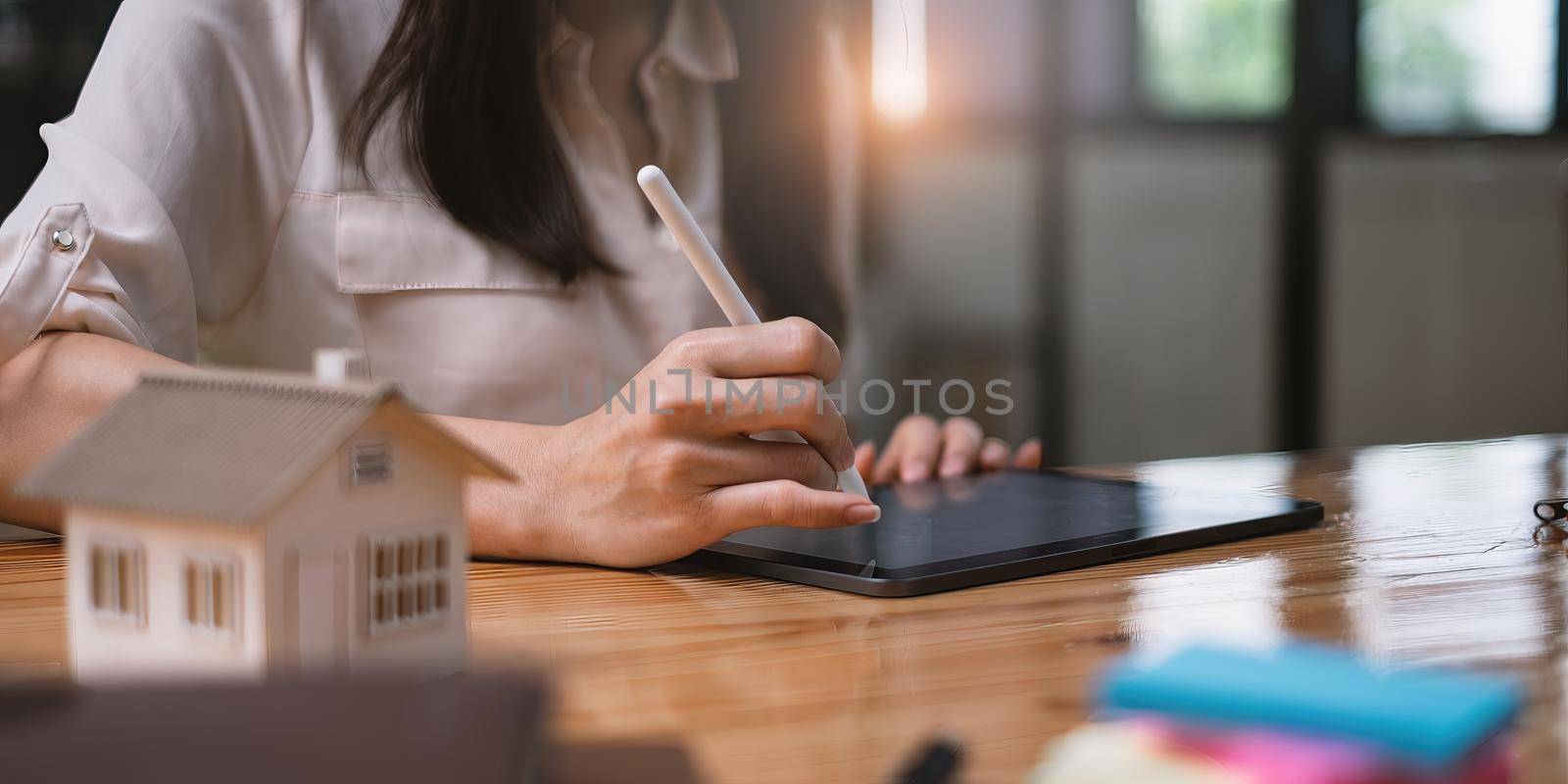 Architect woman using a digital tablet application to hand-draw a design house with a model on a wooden desk. Property idea in real estate. by itchaznong