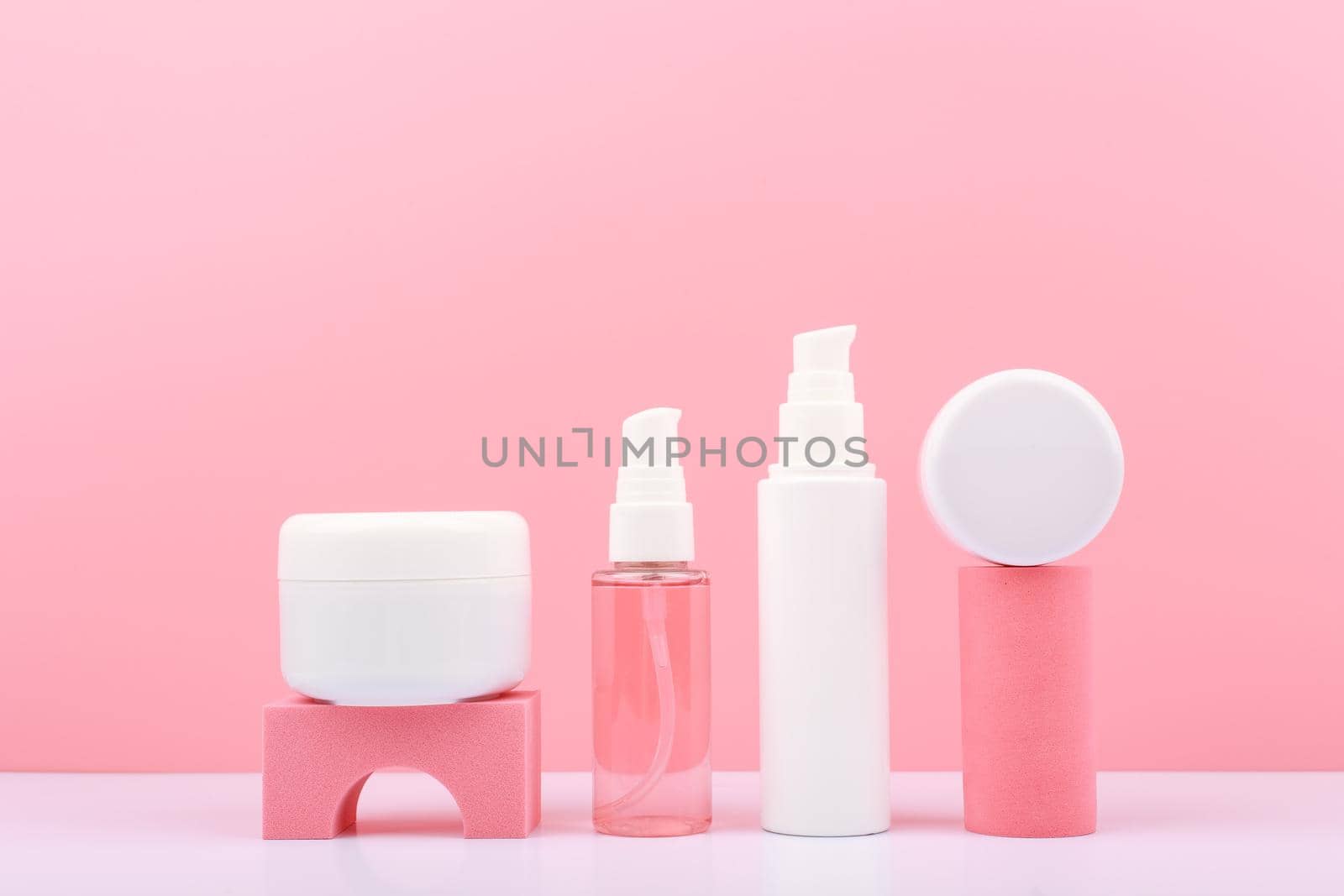 Trendy composition in pink colors with set of cosmetic bottles with beauty products on geometric props against pink background. Concept of organic cosmetics for glowing, young looking skin