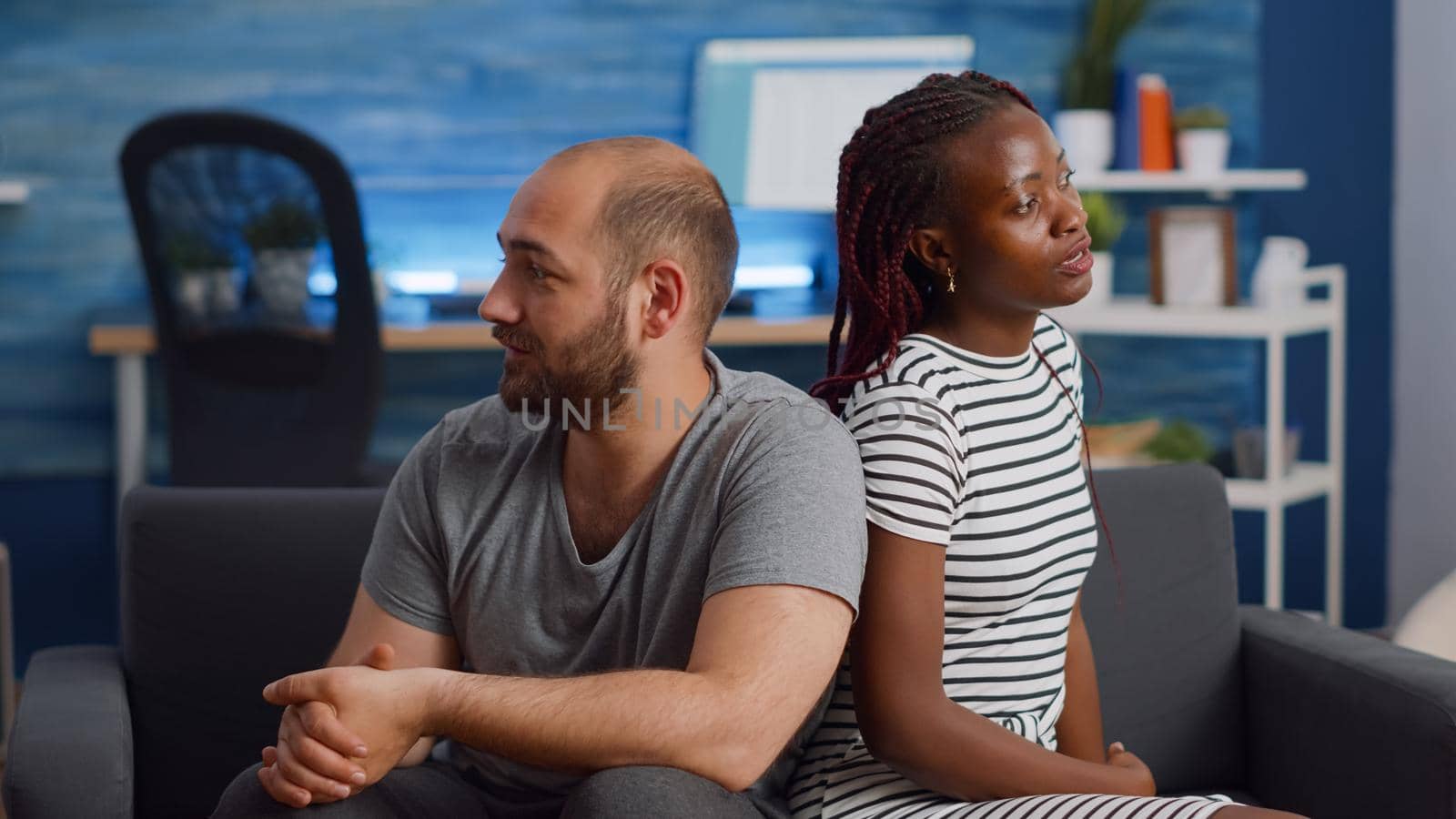 Irritated interracial couple fighting and sitting on couch at home. Multi ethnic lovers having argument yelling in living room. Angry mixed race people with relationship problems shouting
