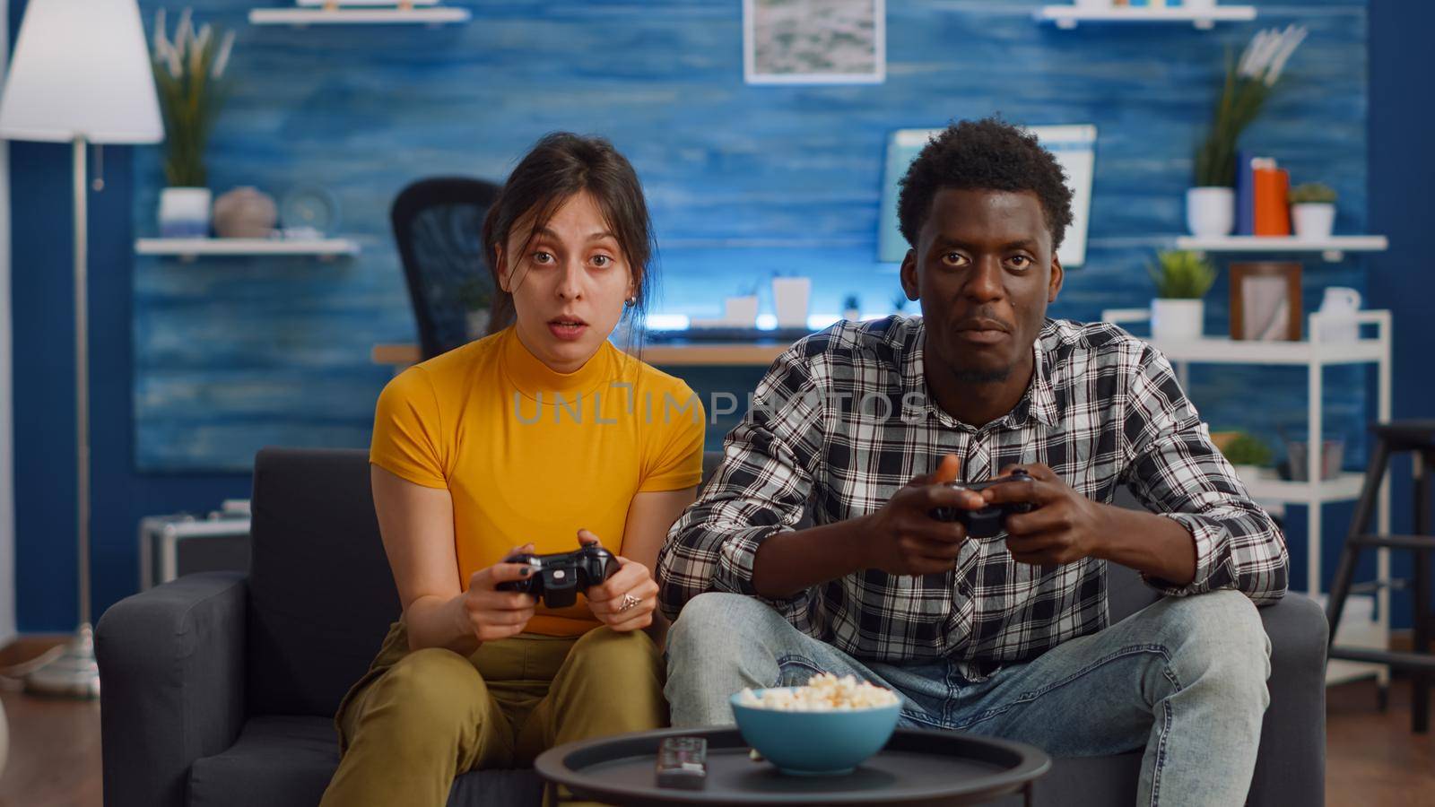 Modern interracial couple playing with joysticks for video game on console in living room. Young mixed race partners doing fun activity with television and controller together at home
