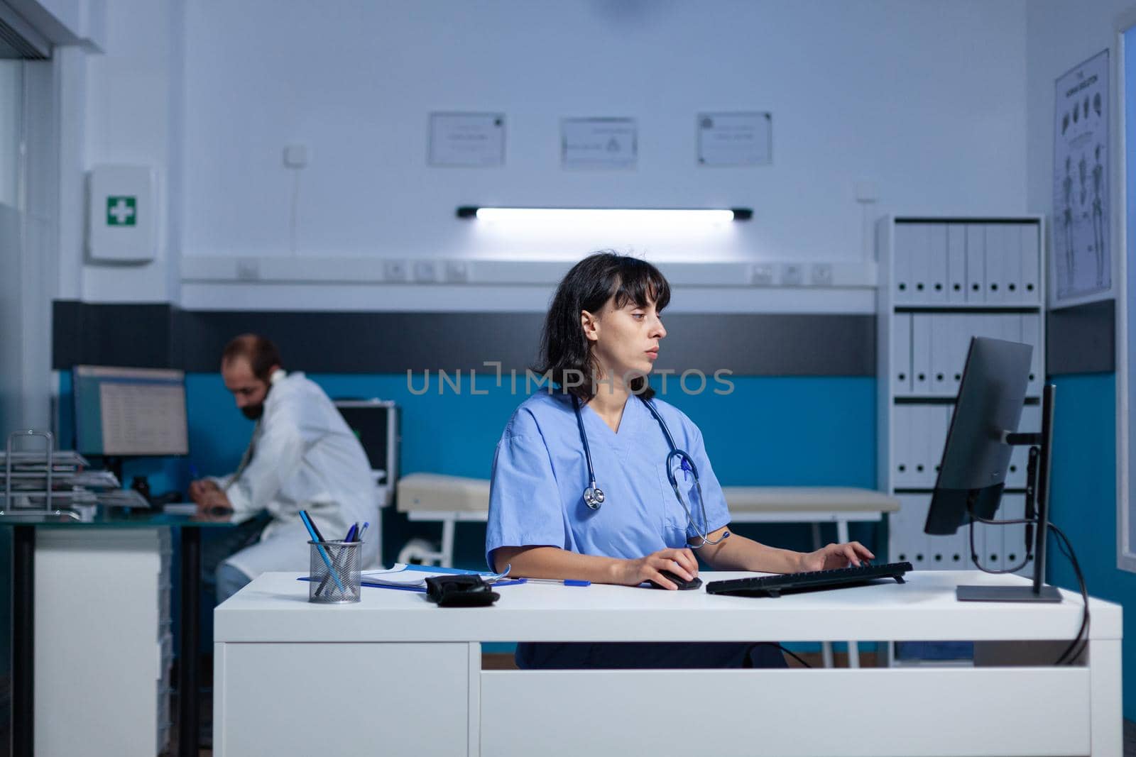 Medical assistant using keyboard and computer at office for healthcare system. Woman nurse looking at monitor screen for assistance and support, working late at night. Health specialist