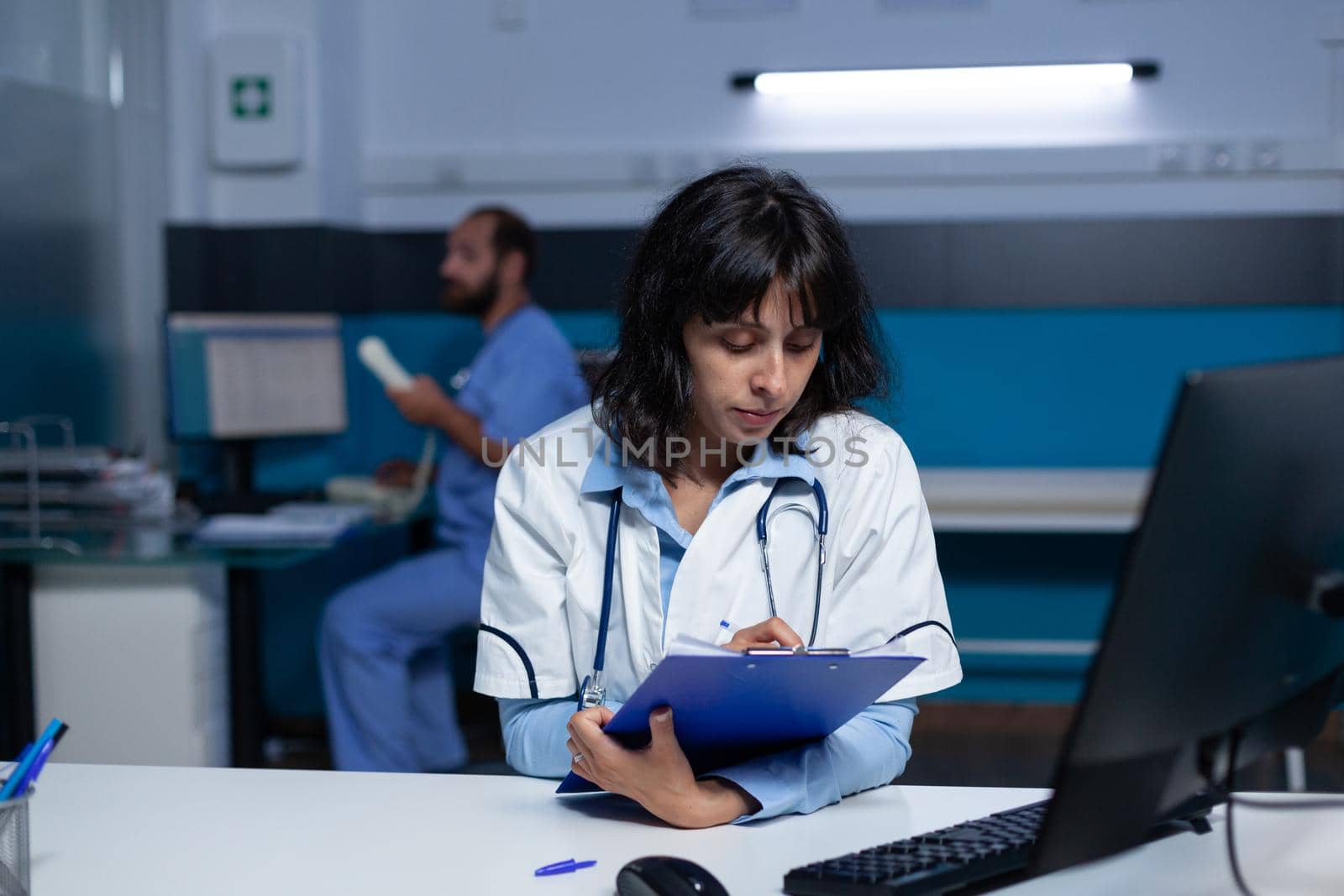 Professional medic looking at computer screen and medical files for healthcare. Doctor analyzing information on monitor and taking notes on papers for assistance, doing overtime work.