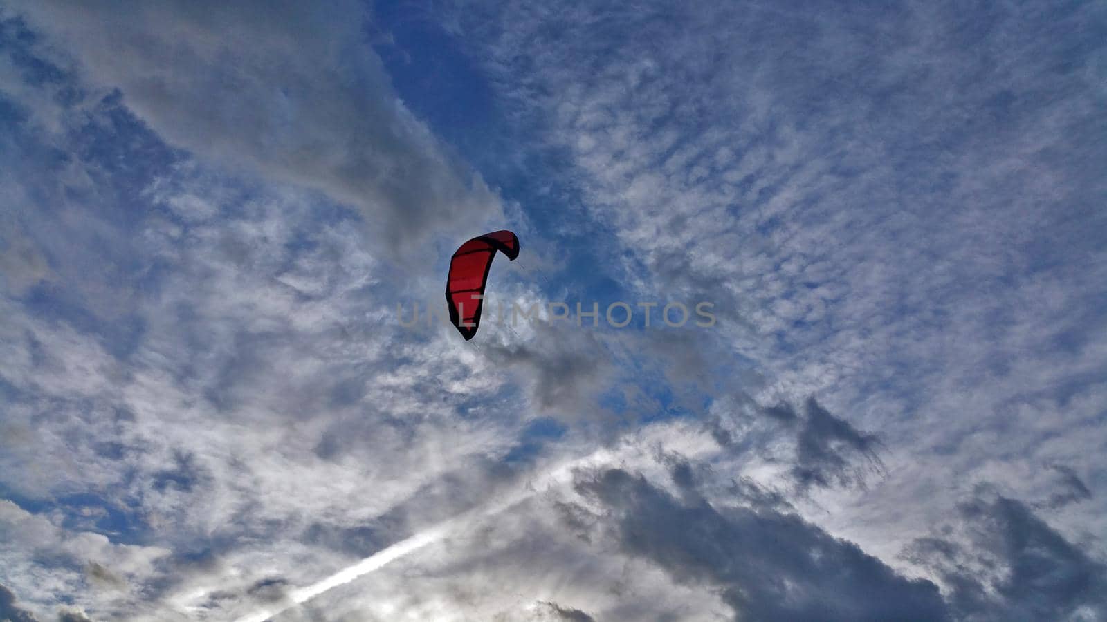Red paraglider on the cloudy sky background.