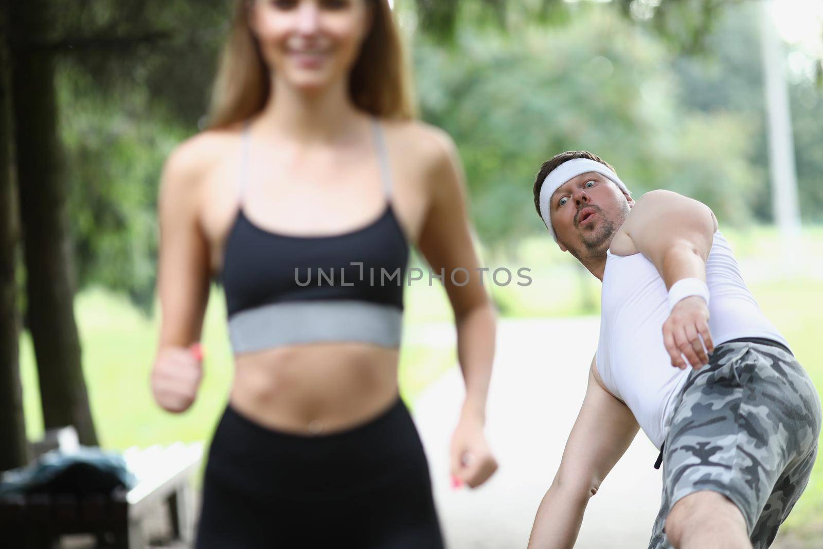 Portrait of tired sweaty middle aged man fall from beauty of young woman. Active woman jogging in front, feeling energetic. Sport, healthy habit concept