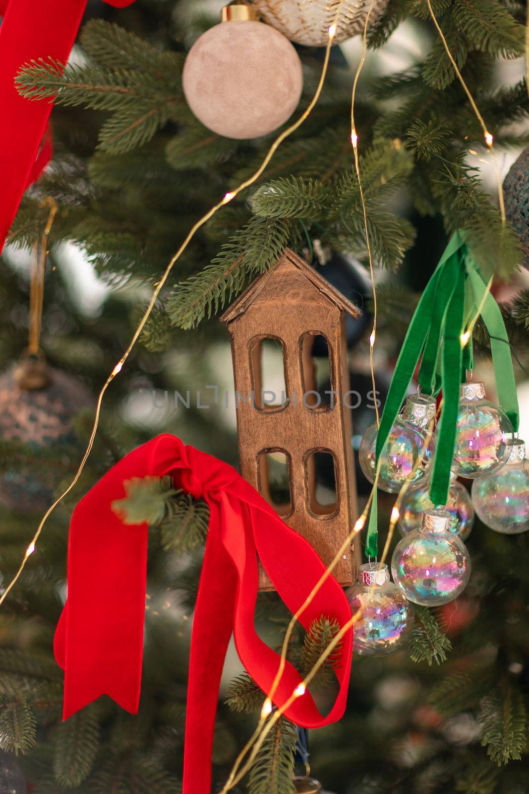 Beautiful decorated christmas tree, red ribbons, balls, wooden house. Merry Christmas and New Year holidays background.