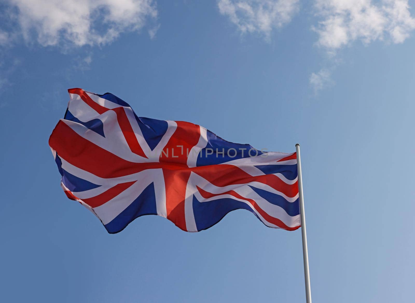 UK Great Britain national flag flying and waving in the wind over clear blue sky, symbol of British patriotism, low angle, side view