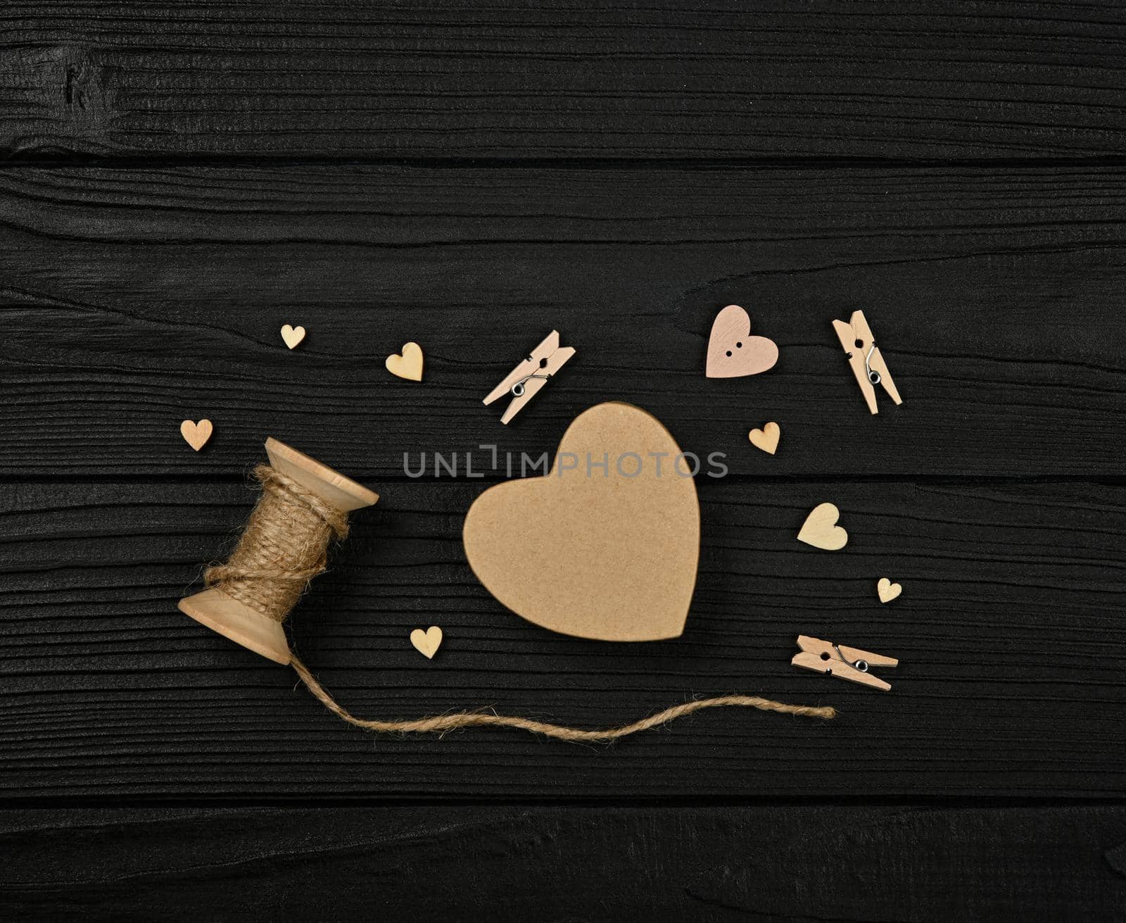 Preparing Valentine gifts, brown paper box, hearts, twine, clothespins on black wooden table background, close up flat lay, elevated top view, directly above